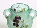 a green vase with purple flowers on it sitting on a table