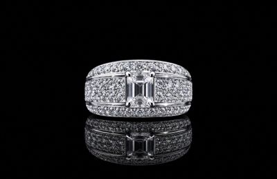 a white gold ring with emeralds and diamonds on a black surface