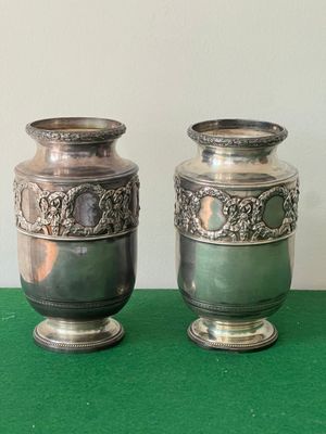 two silver vases sitting next to each other on a green table