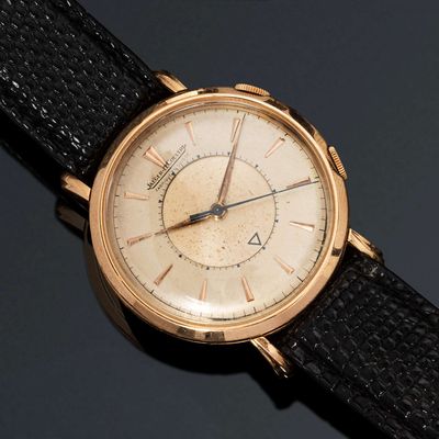 une montre-bracelet en or avec un bracelet noir posée sur un fond noir