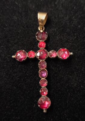 un pendentif en forme de croix en pierre rose posé sur un fond de velours noir