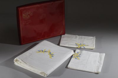 trois serviettes blanches ornées de fleurs bleues et jaunes se trouvent à côté d'une boîte rouge