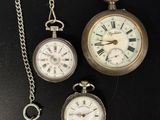 trois types différents de montres de poche posées sur une table, accompagnées d'une clé