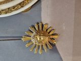 a gold flower brooch on a table next to a white plate