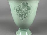 un vase vert orné de fleurs, posé sur une surface grise