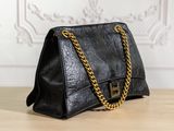 a black leather handbag with gold chains on a wooden table