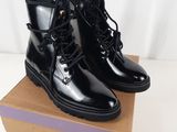 des bottes en cuir noir à lacets, avec des semelles en caoutchouc, posées sur une boîte en carton