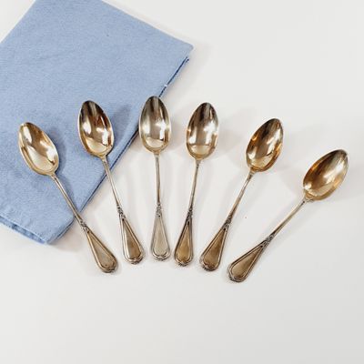six silver spoons and a blue napkin on a white surface