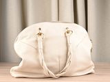 a white purse sitting on a table with a curtain behind it