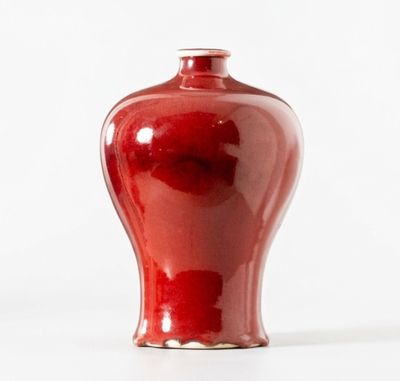 un vase rouge posé sur une surface blanche