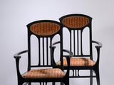 pair of black chairs with wicker seats against a white wall