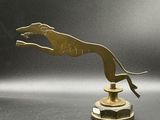 sculpture en laiton représentant un chien sautant par-dessus un socle posé sur une surface grise