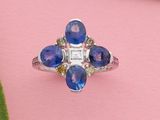un gros plan d'une bague sertie d'un saphir bleu et de diamants, posée sur un fond rose