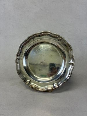 un plat en argent ancien posé sur une table, dans lequel se reflète une personne