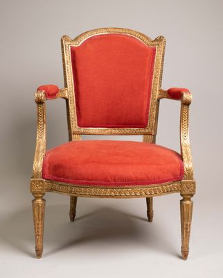 une chaise rouge avec des finitions dorées et une assise rembourrée rouge