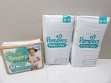 two packs of pampers baby diapers sitting on a table next to a box of diapers