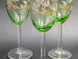 four green wine glasses with white flowers on them sitting next to a coin