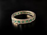 a close up of a gold ring with green stones on a black surface