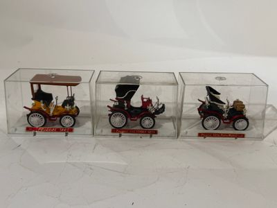 trois petites voitures dans une boîte transparente posée sur une surface blanche