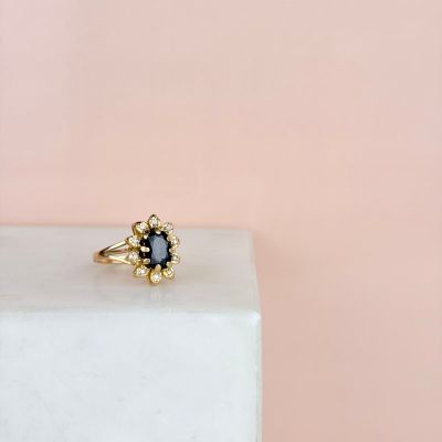 une bague en or sertie d'un saphir bleu, posée sur un bloc de marbre blanc