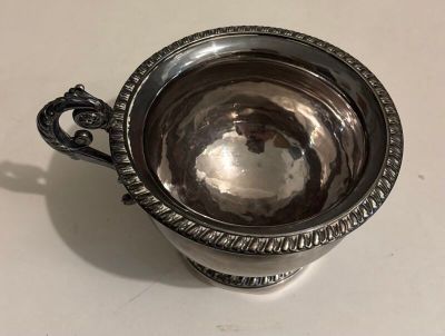 an antique silver cup with a handle on a white table