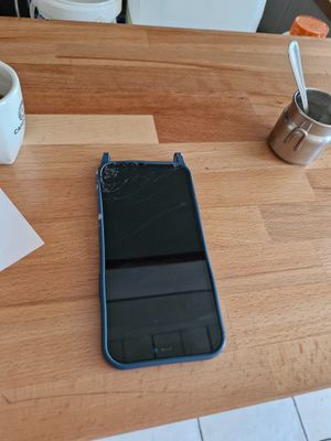 a broken cell phone sitting on a table next to a cup of coffee