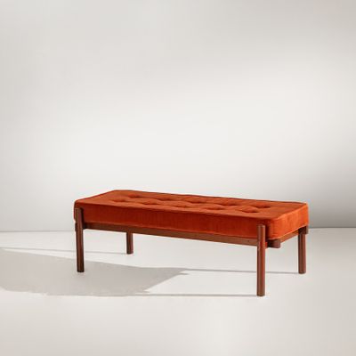 un banc en velours orange avec des pieds en bois, posé sur un sol blanc