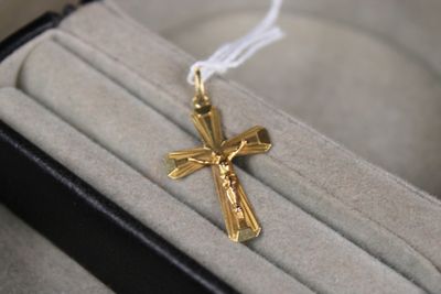 une croix en or suspendue à un cordon blanc, posée sur une boîte noire