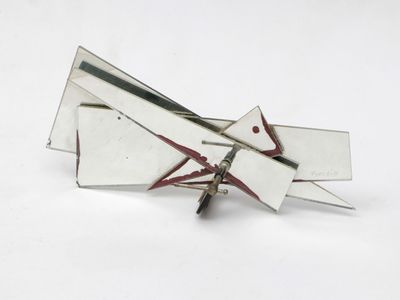 a silver and red brooch on a white surface