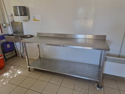 une table en acier inoxydable dans une cuisine où se trouve une poubelle rouge