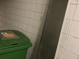 a green trash can sitting in the corner of a bathroom