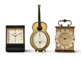 three different clocks and a guitar on a white background