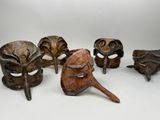 Plusieurs masques en bois sont alignés sur une surface blanche