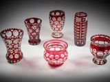 Plusieurs vases en verre rouge sont alignés sur une surface blanche