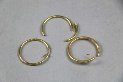 trois paires de boucles d'oreilles créoles en or posées sur une surface blanche