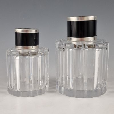 une paire de bouteilles en verre transparent avec des bouchons noirs, posées sur une surface blanche