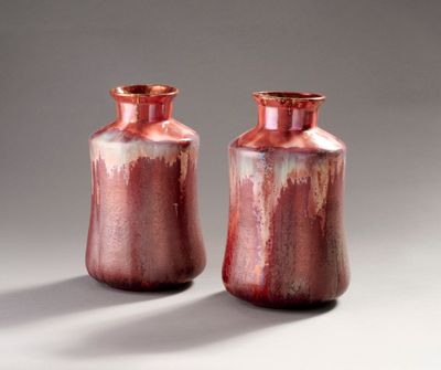 une paire de vases rouges posés sur une table blanche