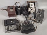 several old cameras are sitting on a white surface with a brown case