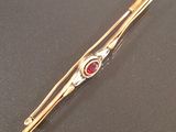 a gold tie bar with a red stone on it