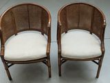 pair of wicker chairs with white cushions on a concrete floor