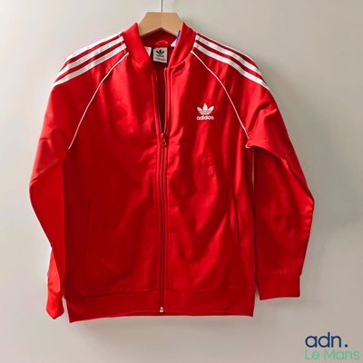 une veste Adidas rouge à rayures blanches suspendue à un cintre