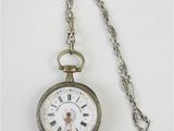 une montre de poche en argent avec une chaîne, posée sur une surface blanche