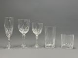 four wine glasses and a glass tumbler are lined up on a table