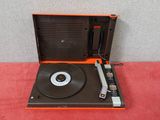 une platine vinyle orange et noire posée sur une table rouge