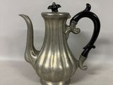 an antique silver coffee pot with a black handle on a white surface