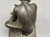 bronze statue of a man sitting on a rock with his back to the camera