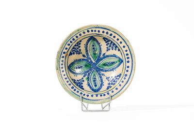 une assiette bleue et verte posée sur un support, sur une surface blanche