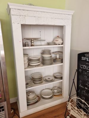 une armoire blanche sur laquelle sont posées des assiettes et un tableau noir posé par terre