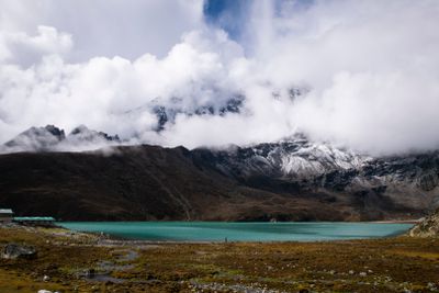 Des nuages recouvrent les montagnes et un lac au premier plan.