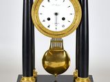 une horloge noire et dorée posée sur un socle, sur fond blanc